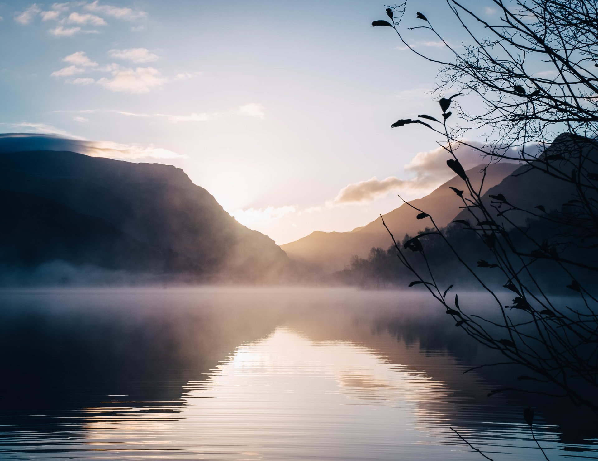 See mit Nebel und Sonnenaufgang zwischen Bergen